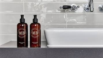 Two bottles of hand wash and body lotion on a bathroom counter next to a white bathtub with a chrome faucet.
