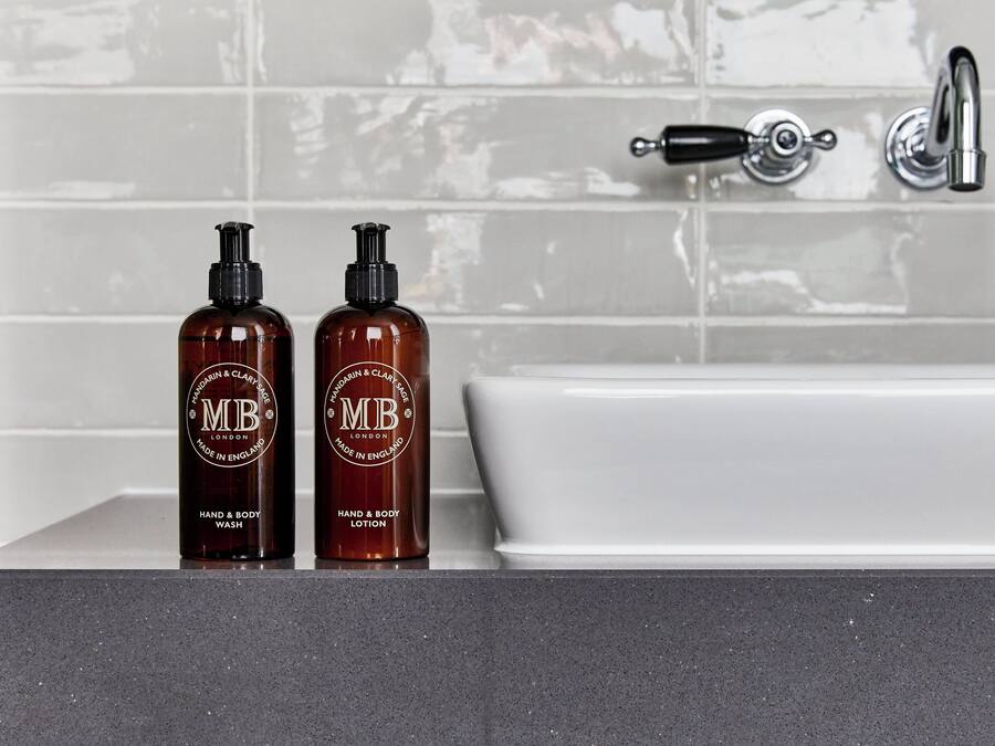 Two bottles of hand wash and body lotion on a bathroom counter next to a white bathtub with a chrome faucet.
