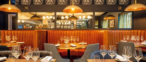 A restaurant interior with booths, tables, and hanging pendant lights.