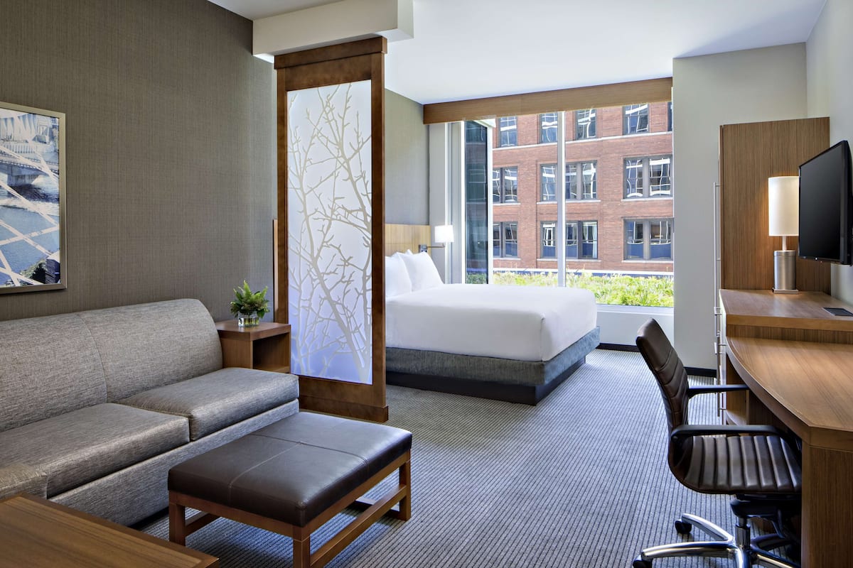A hotel room with a bed, sofa, desk, and TV.