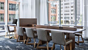 Una sala de conferencias moderna con una larga mesa y seis sillas, ventanas amplias con cortinas, y vistas a un paisaje urbano.