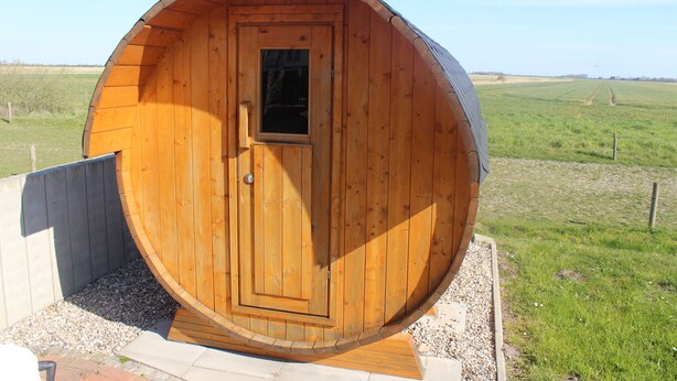 A wooden barrel-shaped structure with a door and window, surrounded by gravel and grass. - Viola Tricolor, Exclusive FW on North Beach, pure relaxation, hiking, biking (Nordstrand)