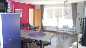 A modern kitchen with a dining area, a microwave, a table with chairs, and a window with curtains. - Viola Tricolor, Exclusive FW on North Beach, pure relaxation, hiking, biking (Nordstrand)