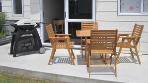 Une terrasse extérieure avec une table et des chaises en bois, un barbecue et une porte-fenêtre coulissante donnant sur un garage.