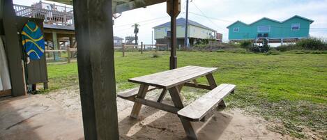 Una mesa de picnic de madera bajo una zona techada, con vistas a casas y un campo cubierto de césped.