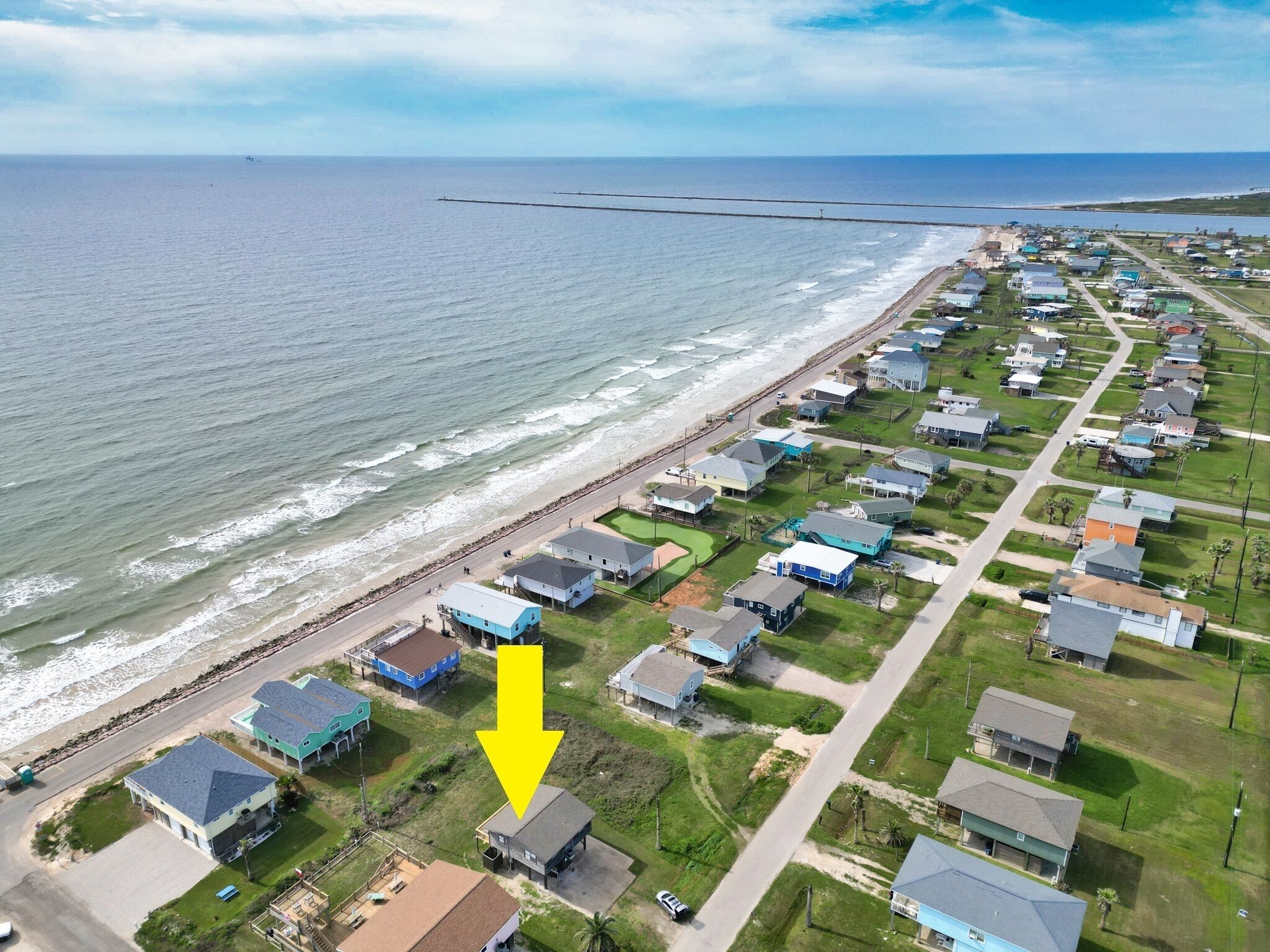 Zona residencial costera con casas alineadas a lo largo de la playa, con una combinación de edificios de uno y dos pisos, algunos con garajes adjuntos.