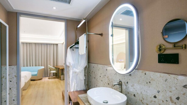 A modern bathroom with a large oval sink, a round mirror, and a robe hanging on a rack.