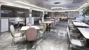A modern restaurant interior with marble flooring, round tables, and cushioned chairs.