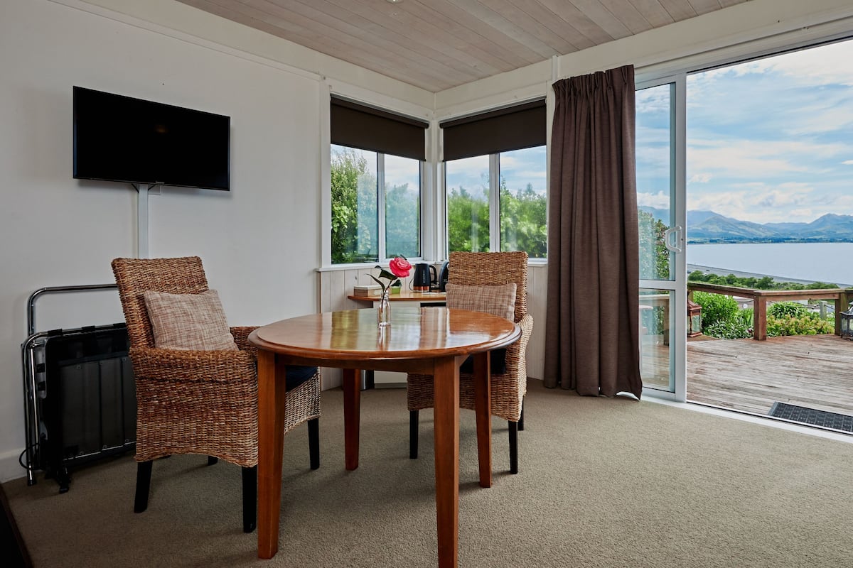 A room with a wooden table and chairs, a flat-screen TV, a window with a view of the outdoors, and a sliding glass door.