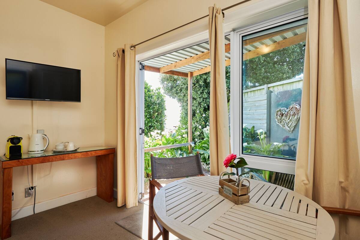 A room with a TV mounted on the wall, a wooden table with a flower vase, and a window with curtains.