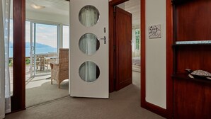 A room with a large glass door leading to a balcony with a view of the sea and mountains.
