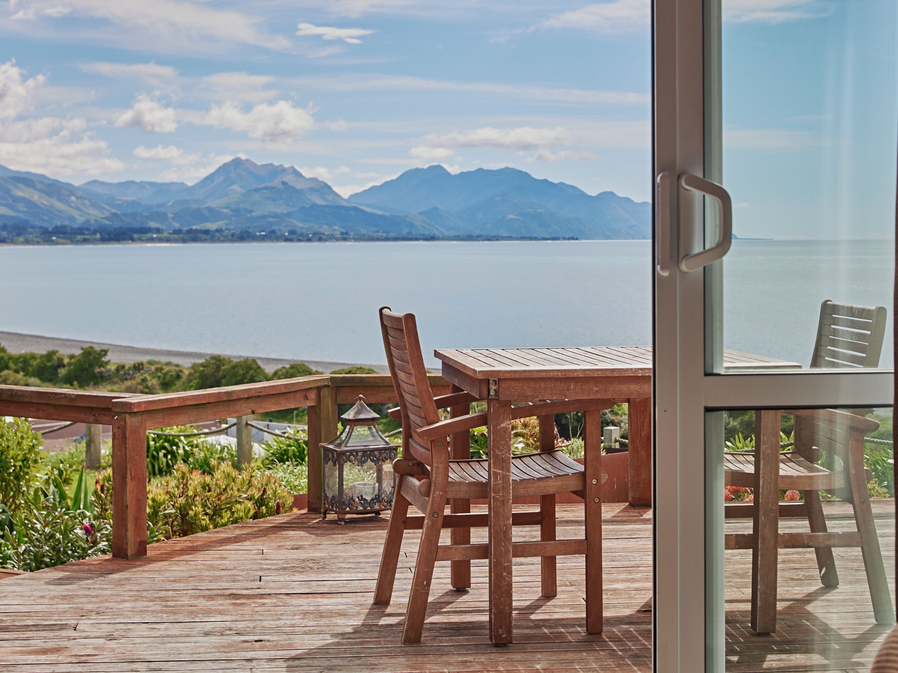A wooden deck with a table and chairs overlooking a lake and mountains.
