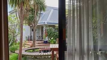 Una terraza de madera con una mesa y sillas, rodeada por un jardín con una palmera y una casa al fondo.