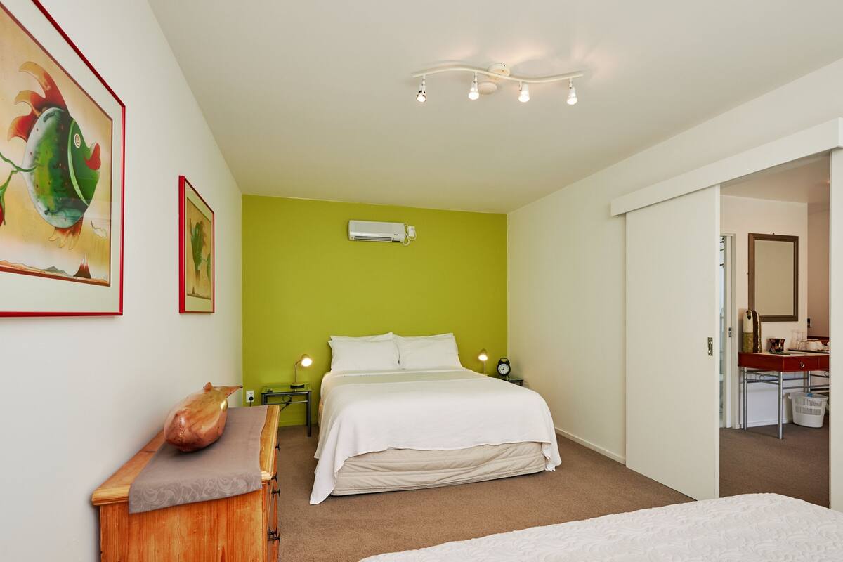 A bedroom with a bed, a dresser, a nightstand, an air conditioner, and a door leading to another room.