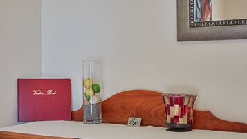 A wooden headboard with a framed mirror, a red book titled "Visitors Book," a clear vase with fruits and a candle, and a striped candle holder.