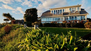 A modern two-story house with a large balcony, surrounded by lush greenery and a well-maintained lawn.