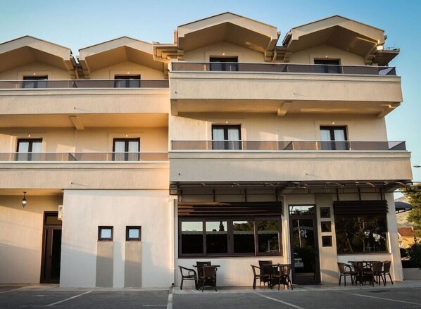 Ein mehrgeschossiges Hotel mit schlichter Fassade, Balkonen und einer überdachten Außenbereich-Sitzgelegenheit.