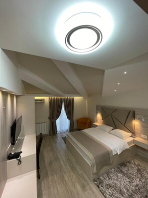 A modern bedroom with a bed, bedside tables, a TV, and a ceiling light. - Hotel Holiday (Podgorica)