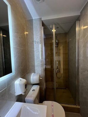 A modern bathroom with a glass-enclosed shower, a toilet, and a hand dryer. - Hotel Holiday (Podgorica)