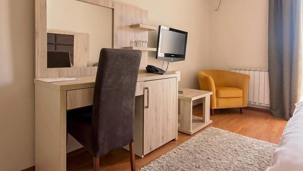 Une chambre d’hôtel avec un bureau en bois, une chaise, un téléviseur et une petite table d’appoint.