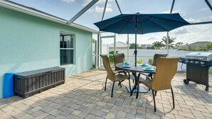 Una terrazza esterna con tavolo e sedie, un barbecue e una zona riparata con ombrellone.