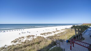 Een strand met wit zand, een helderblauwe lucht en een houten vogel kijken naar strandstoelen en parasols.