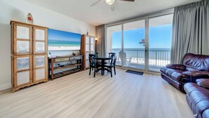 Een woonkamer met een leren bank, een eettafel met stoelen, een houten kast met glazen deuren en een plafondventilator.