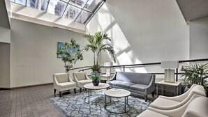A spacious lounge area with a high ceiling and skylight, featuring a grey sofa, white armchairs, and a patterned rug. - Downtown Honolulu Suite Near Ala Moana Beach! (Honolulu)