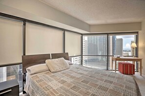 Una moderna camera d'hotel con un letto grande, una scrivania e vista sulla città tramite finestre a tutta altezza.