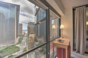 Camera d'albergo in un grattacielo con una grande finestra che si affaccia sulla città, un piccolo tavolino con una lampada e un pouf a righe rosse.