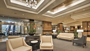 A modern lobby with a central reception desk, seating area, and an escalator in the background. - Downtown Honolulu Suite Near Ala Moana Beach! (Honolulu)