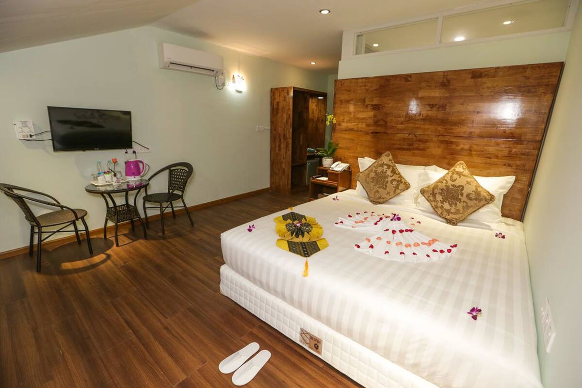 A hotel room with a bed, a TV, a desk with a chair, and a wooden headboard.