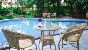 A pool area with wicker chairs and a table, surrounded by greenery. - Grand Garden Hotel Yangon (Yangon)