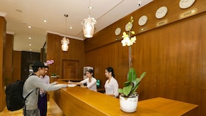 A reception desk with a wooden finish, a potted plant, and clocks indicating different time zones. - Grand Garden Hotel Yangon (Yangon)
