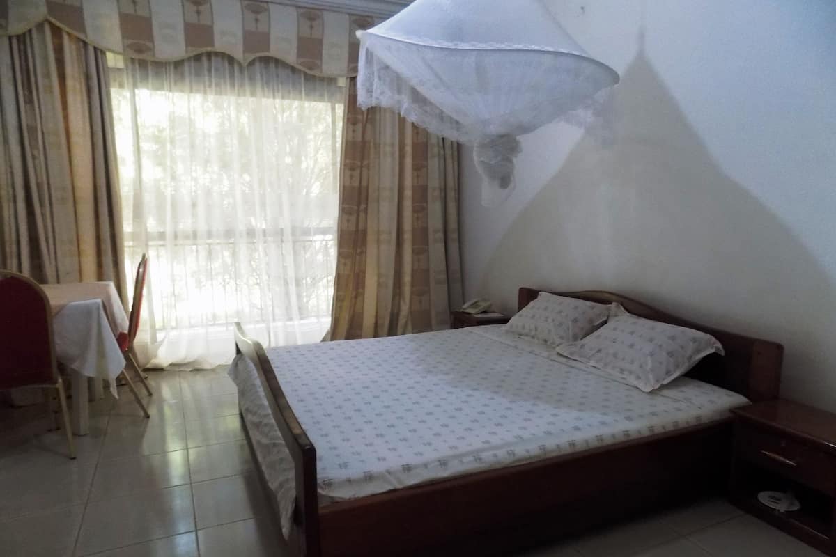 A bedroom with a wooden bed, a bedside table, a chair, a table, and a window with curtains.