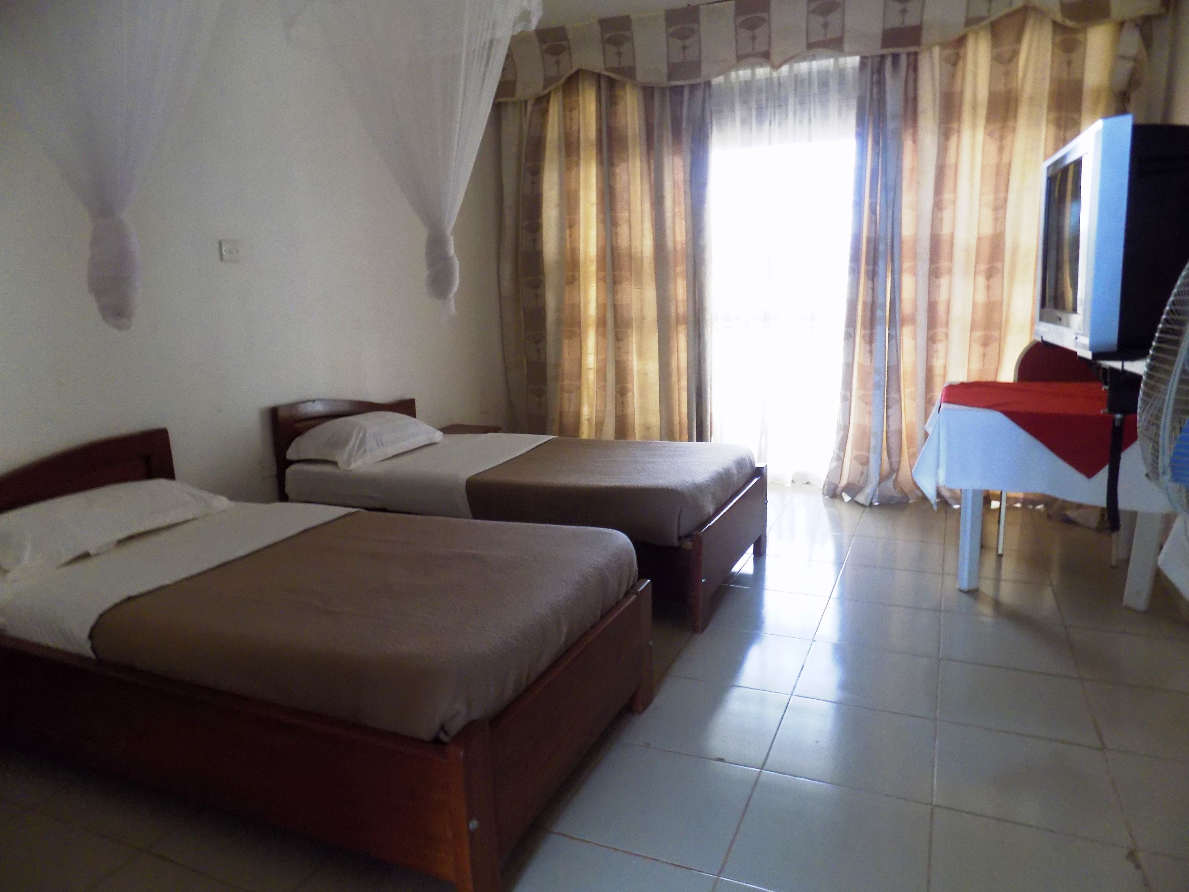 A room with two single beds, a small table with a red cloth, and a window with curtains.
