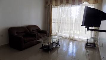 Una sala de estar con un sofá marrón, una mesa de centro de vidrio y un televisor sobre un mueble.