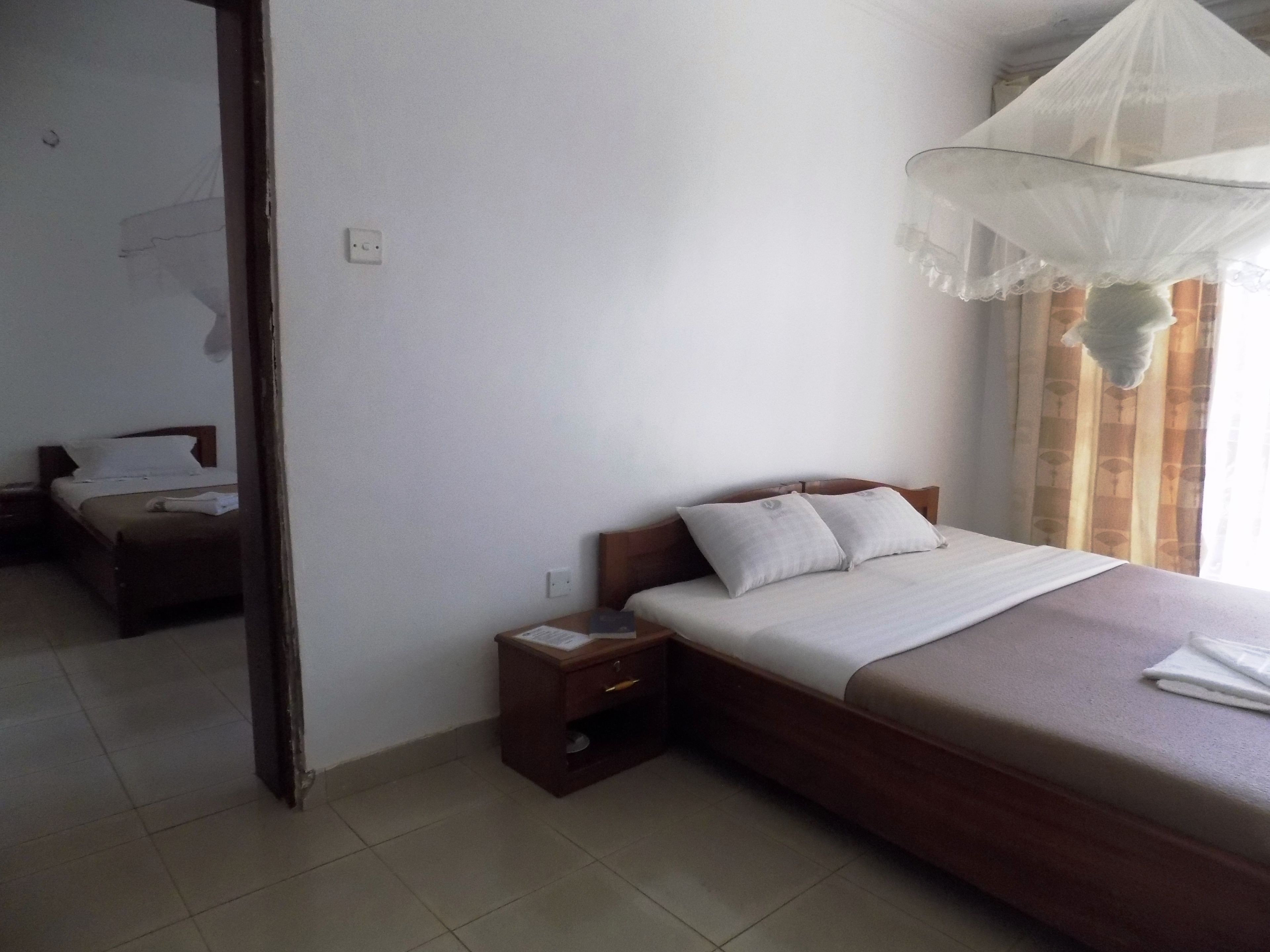 Una habitación de hotel con cama, mesita de noche, espejo y ventana con cortinas.
