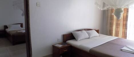 Una habitación de hotel con cama, mesita de noche, espejo y ventana con cortinas.