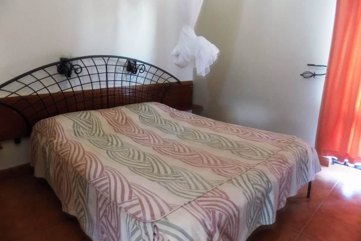 A bed with a patterned bedspread, a mosquito net, and a wooden headboard.