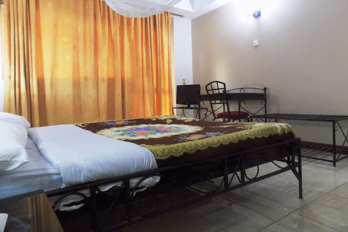 A hotel room with a bed, a desk, a chair, and a curtain.