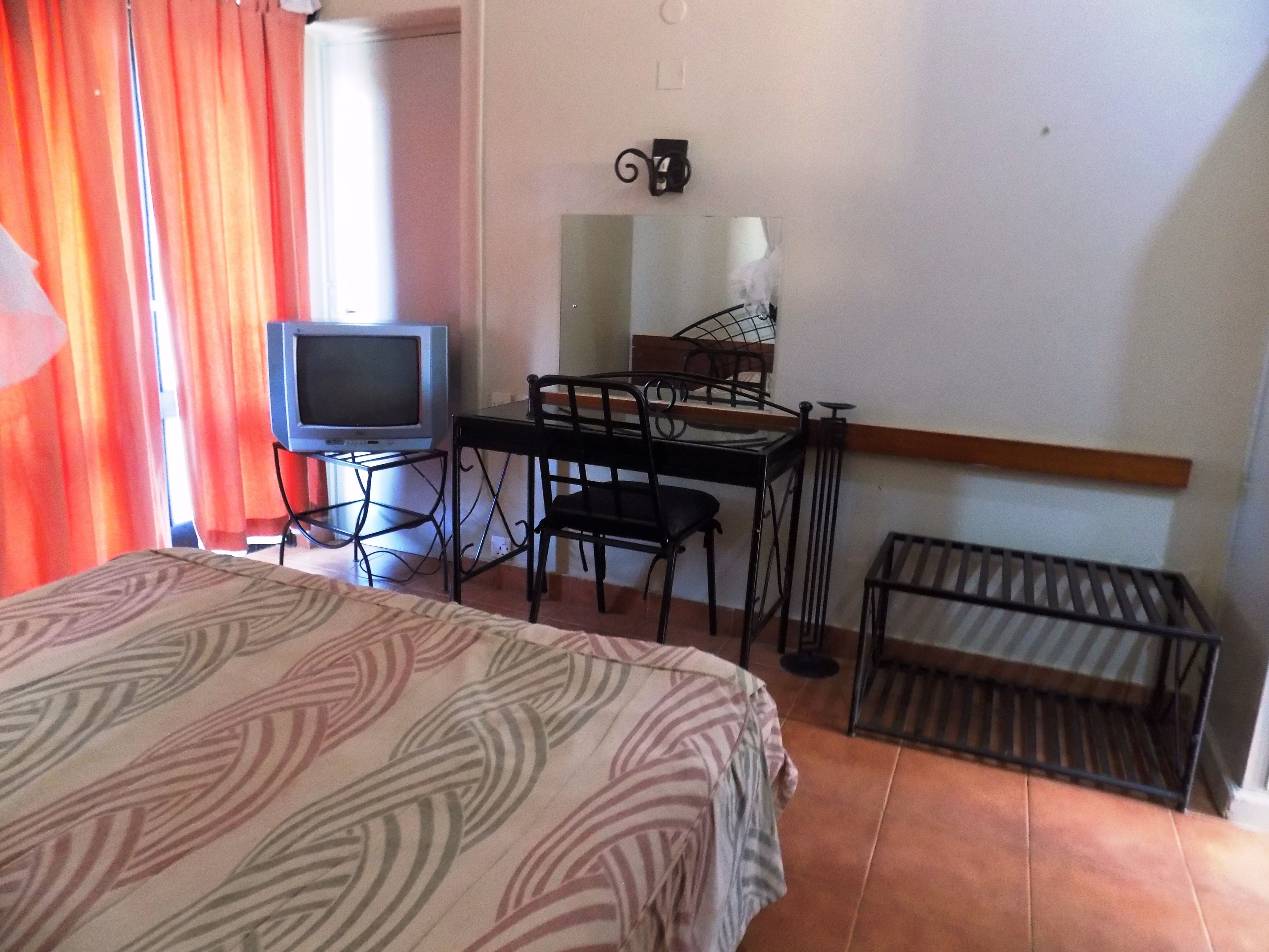 Una habitación de hotel con cama, escritorio, silla, televisión y ventana con cortinas.