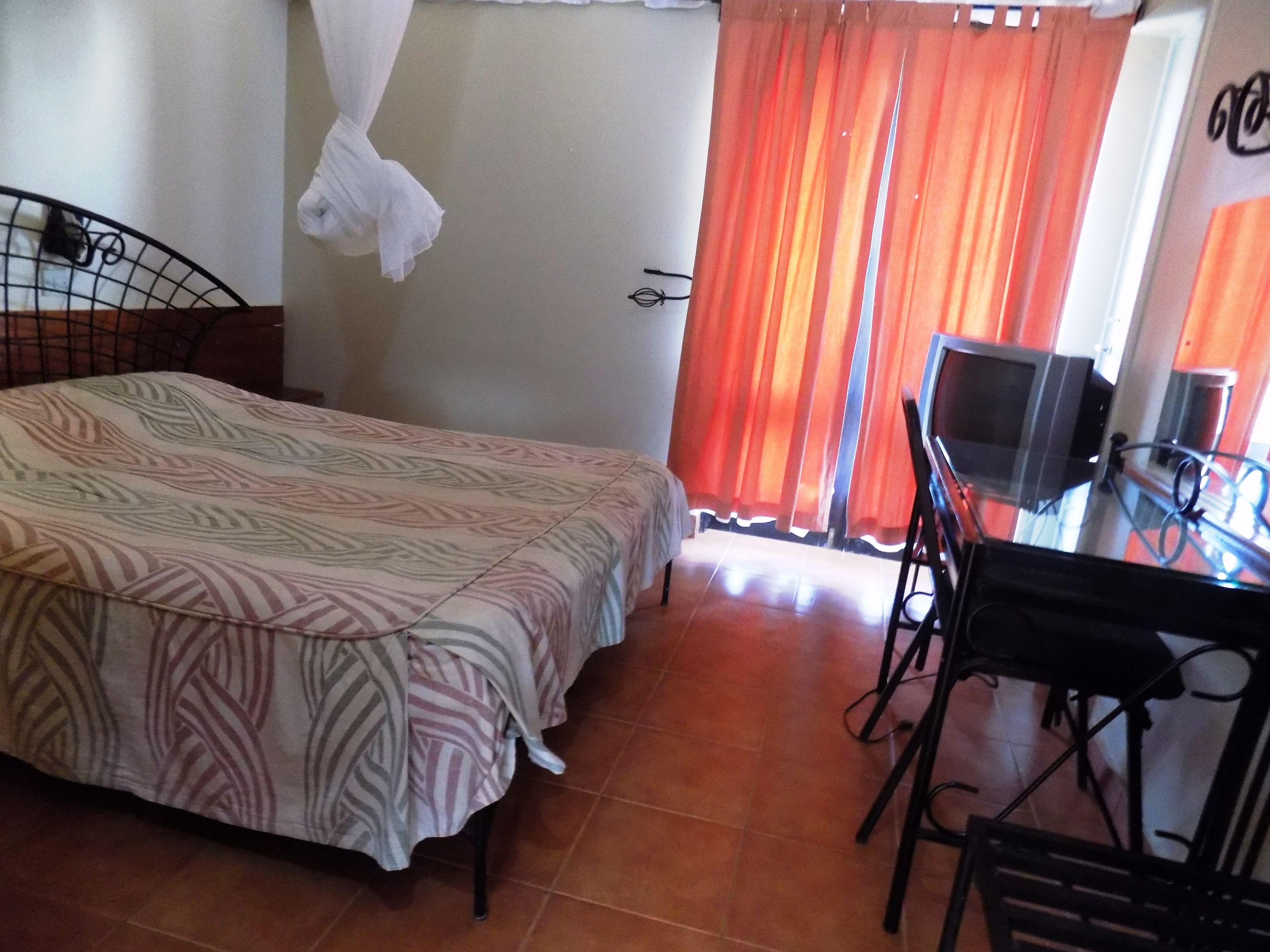 A room with a bed, a TV on a table, and a window with curtains.
