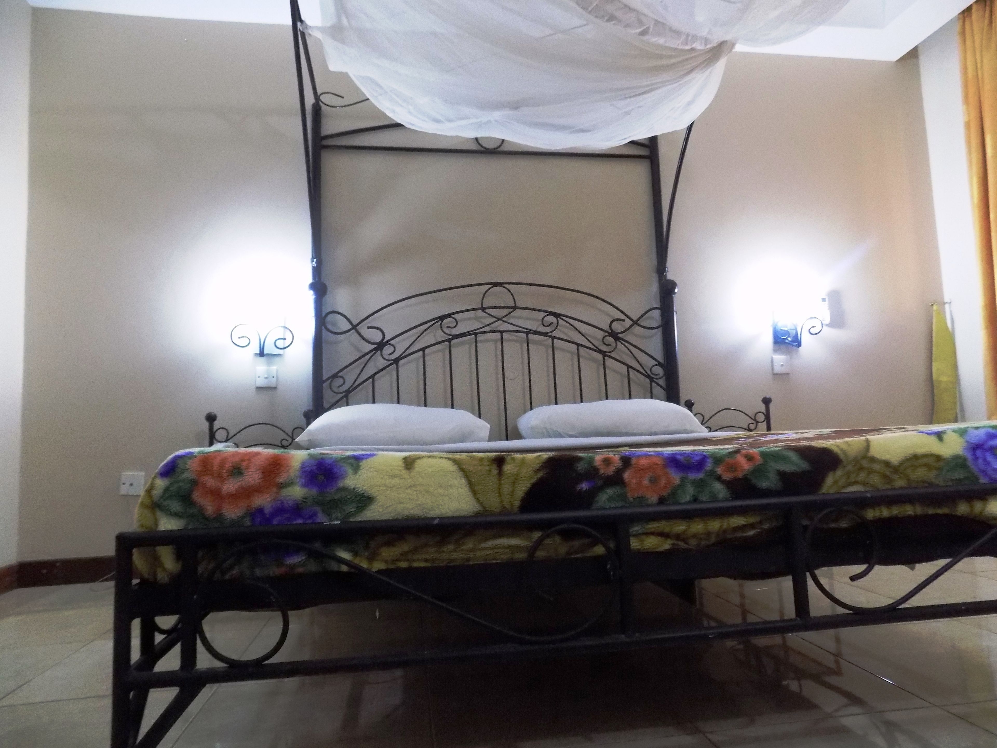 A bed with a metal frame and a canopy, a floral bedspread, and two wall-mounted lights.