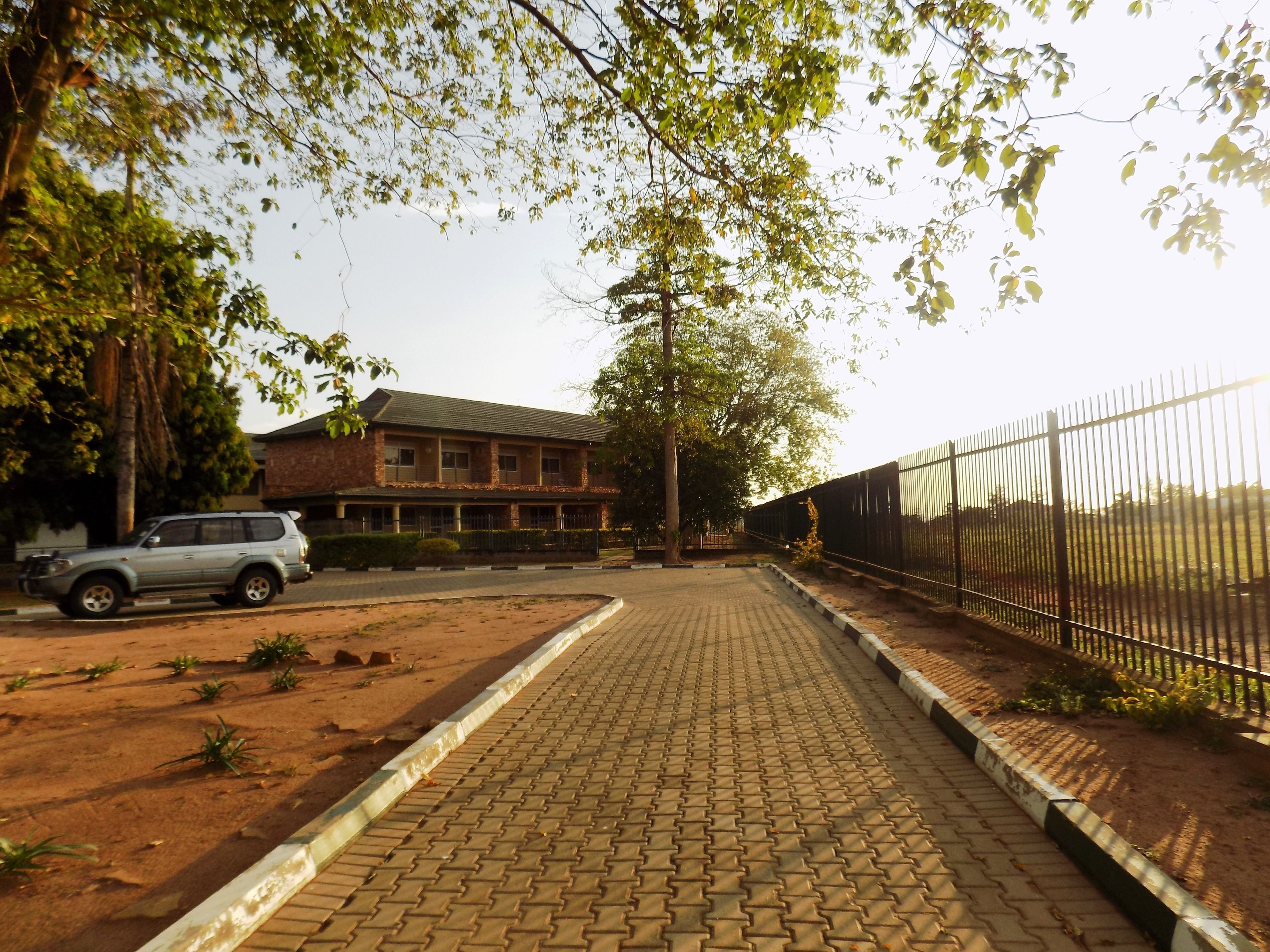 Un camino pavimentado que conduce a un edificio con fachada de ladrillo y una cerca de metal en un lateral.