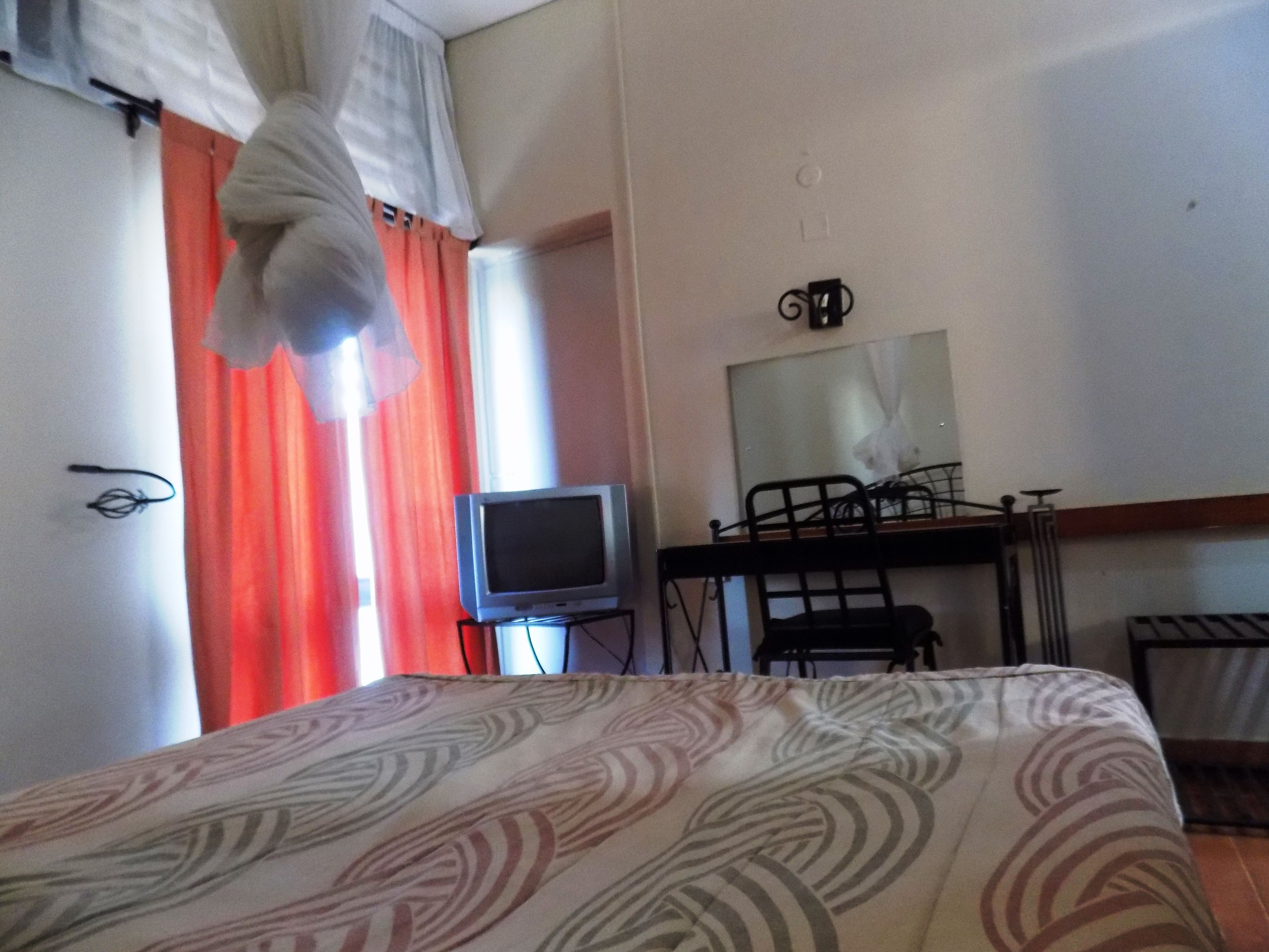 Habitación de hotel con cama, televisor sobre un soporte, escritorio y silla.