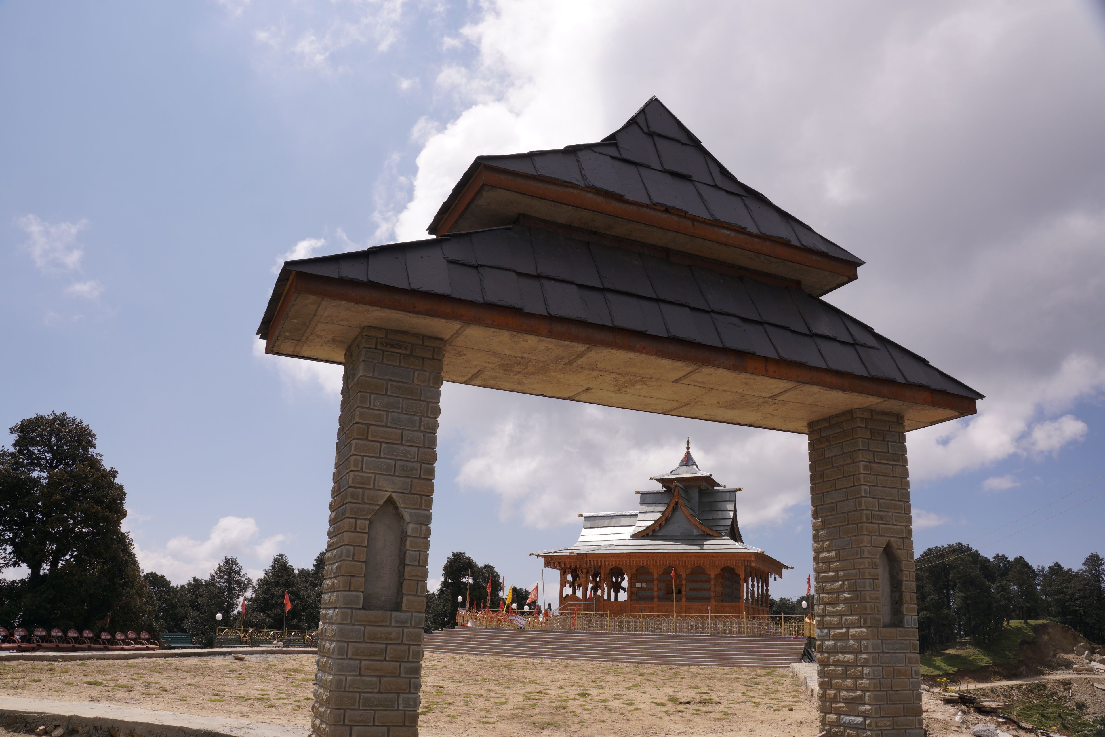 Un pabellón tradicional con tejado de baldosas y pilares de ladrillo, que conduce a un templo con tejado al estilo pagoda.