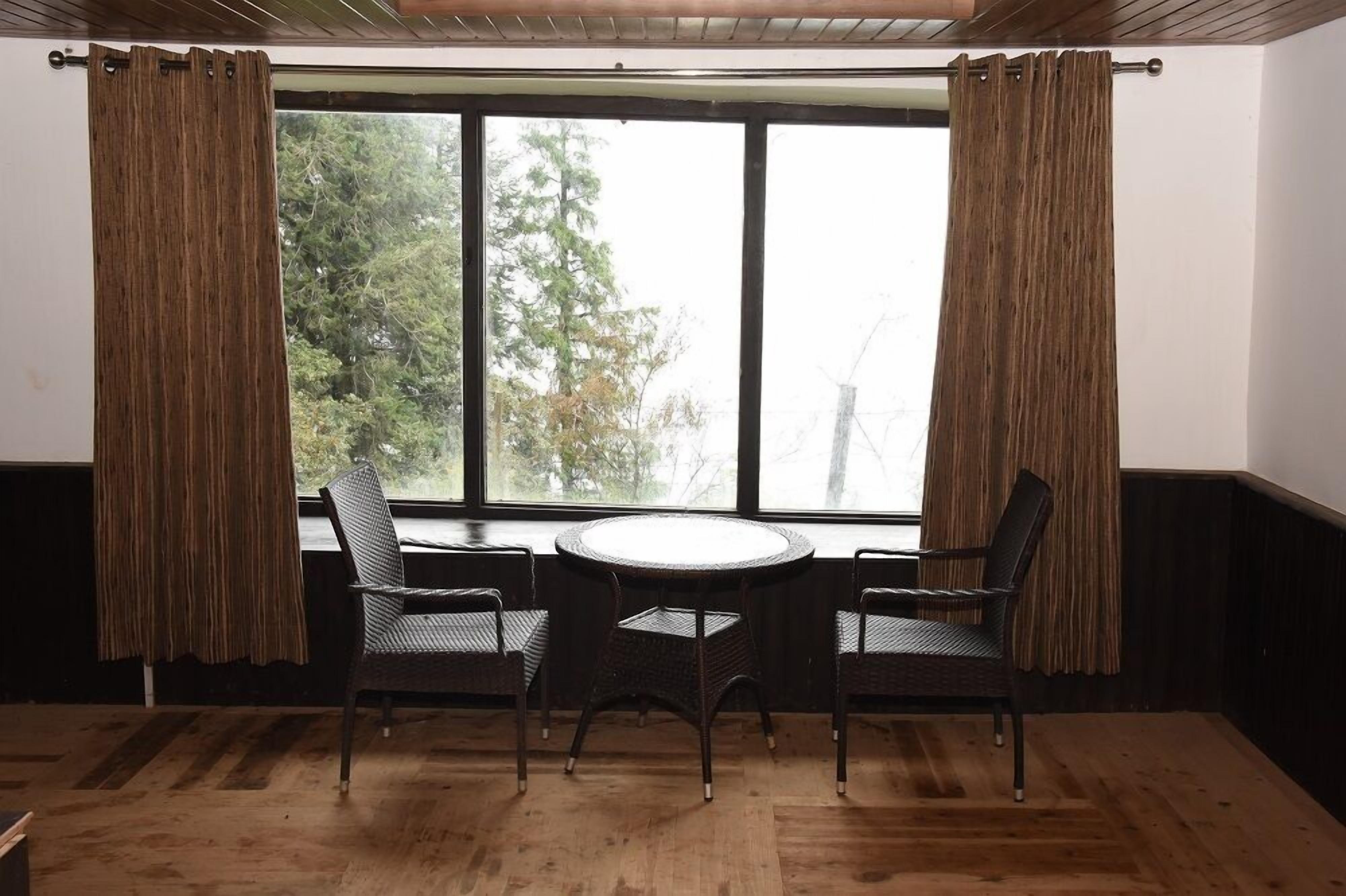 A room with a large window, two wicker chairs, and a round table.