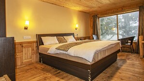 Quarto com painéis de madeira, uma cama grande, duas luzes fixadas na parede e uma janela vista para árvores.