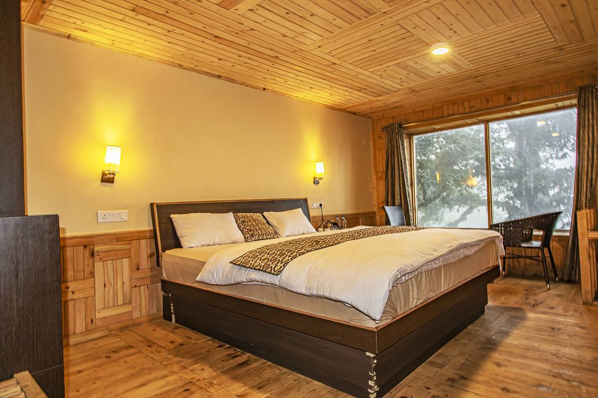 A wooden-paneled bedroom with a large bed, two wall-mounted lights, and a window with a view of trees.
